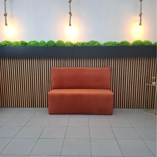 Banco corrido estofado em veludo laranja, junto a uma parede ripada